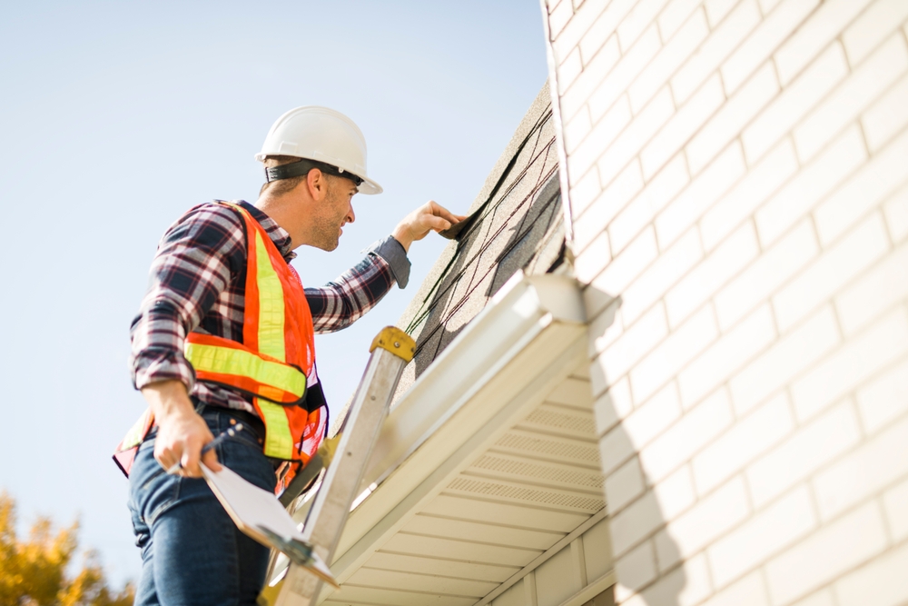 Roof Repair 1 A man with hard hat standing on steps inspecting house roof