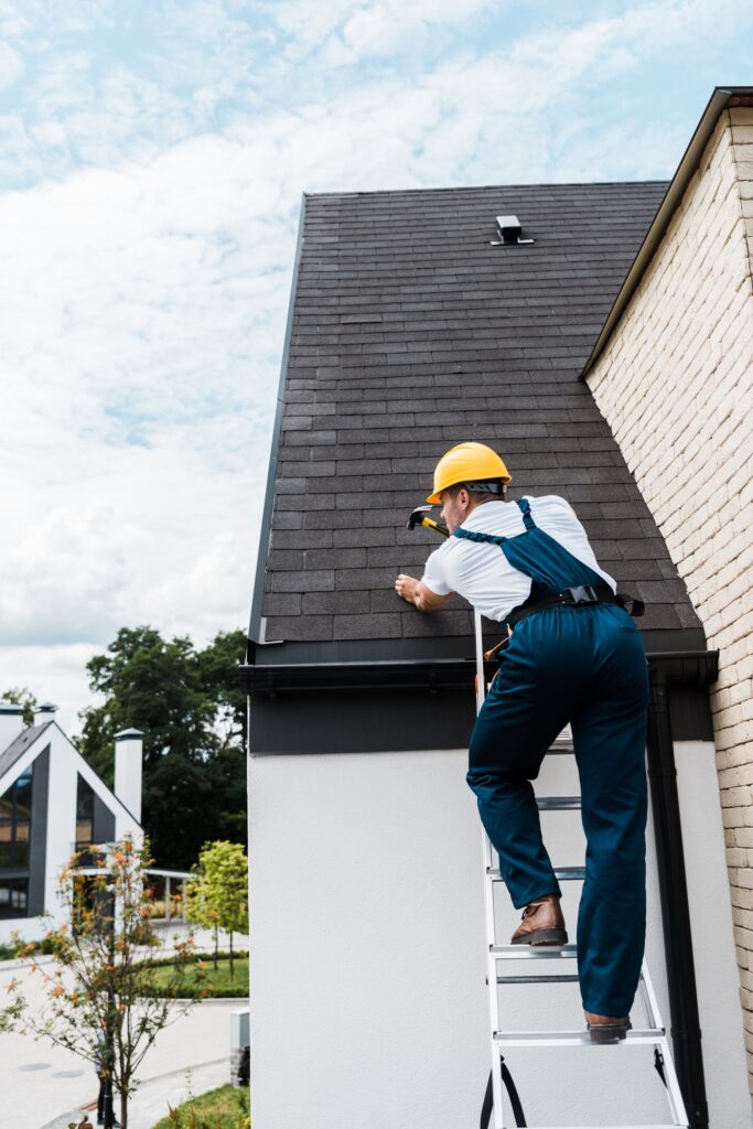Roof Repair 6 repairman in uniform and helmet repairing roof while standing on ladder
